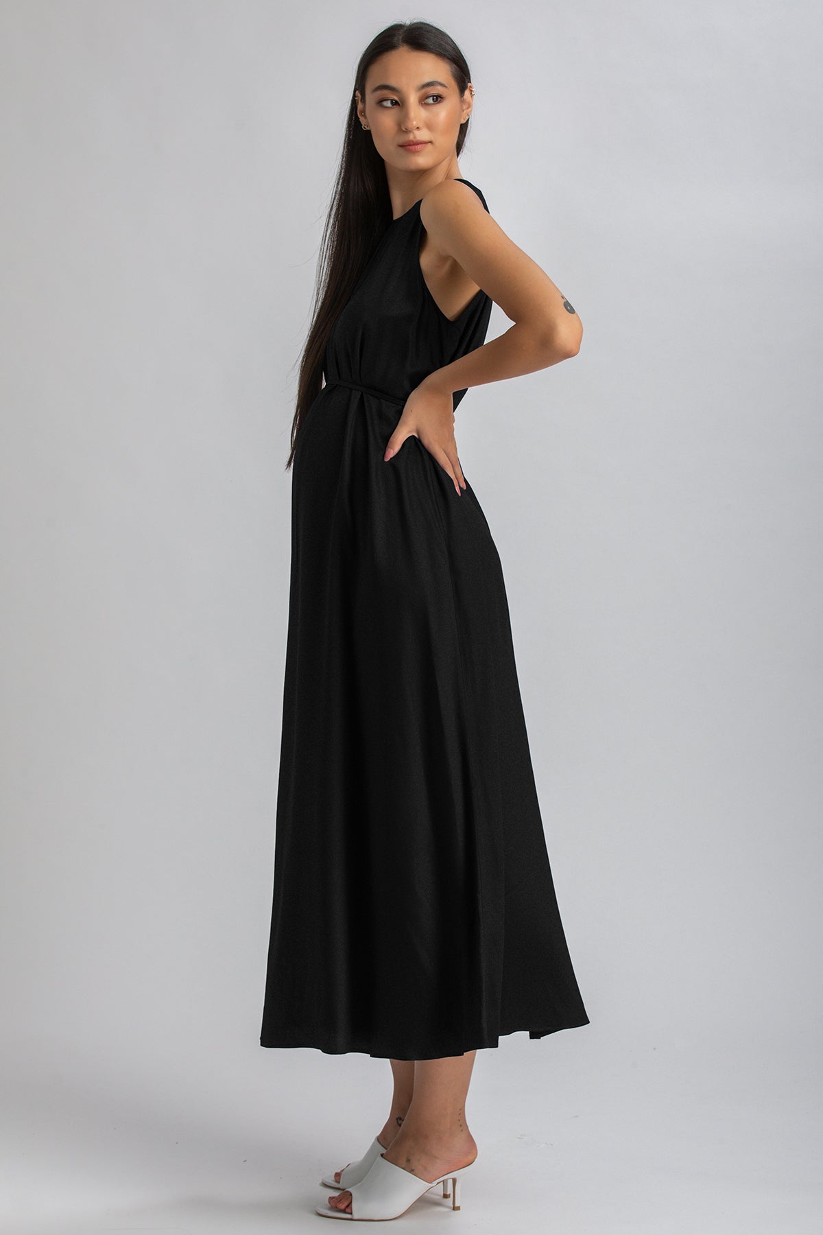 Donna incinta con abito premaman nero lungo elegante, sfondo neutro.