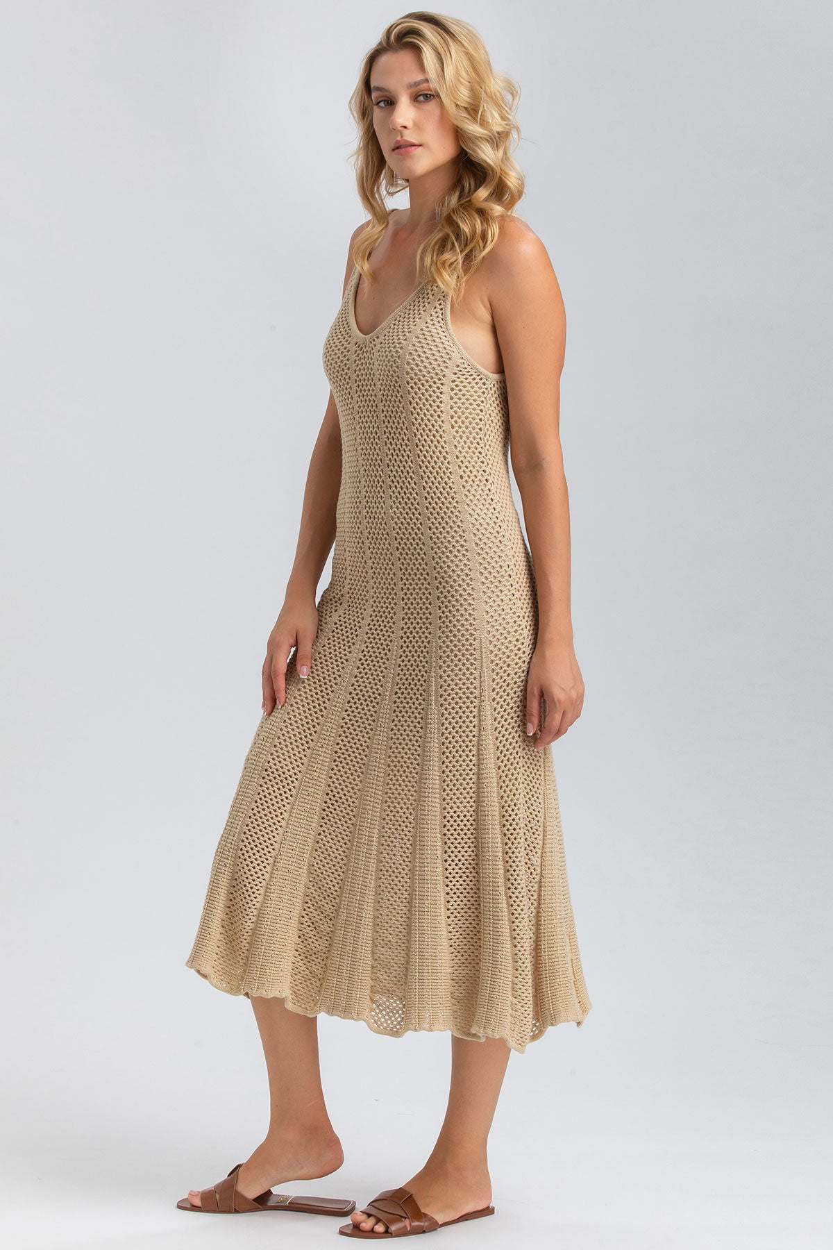Donna con abito premaman beige in maglia traforata, sandali bassi, fondo neutro.