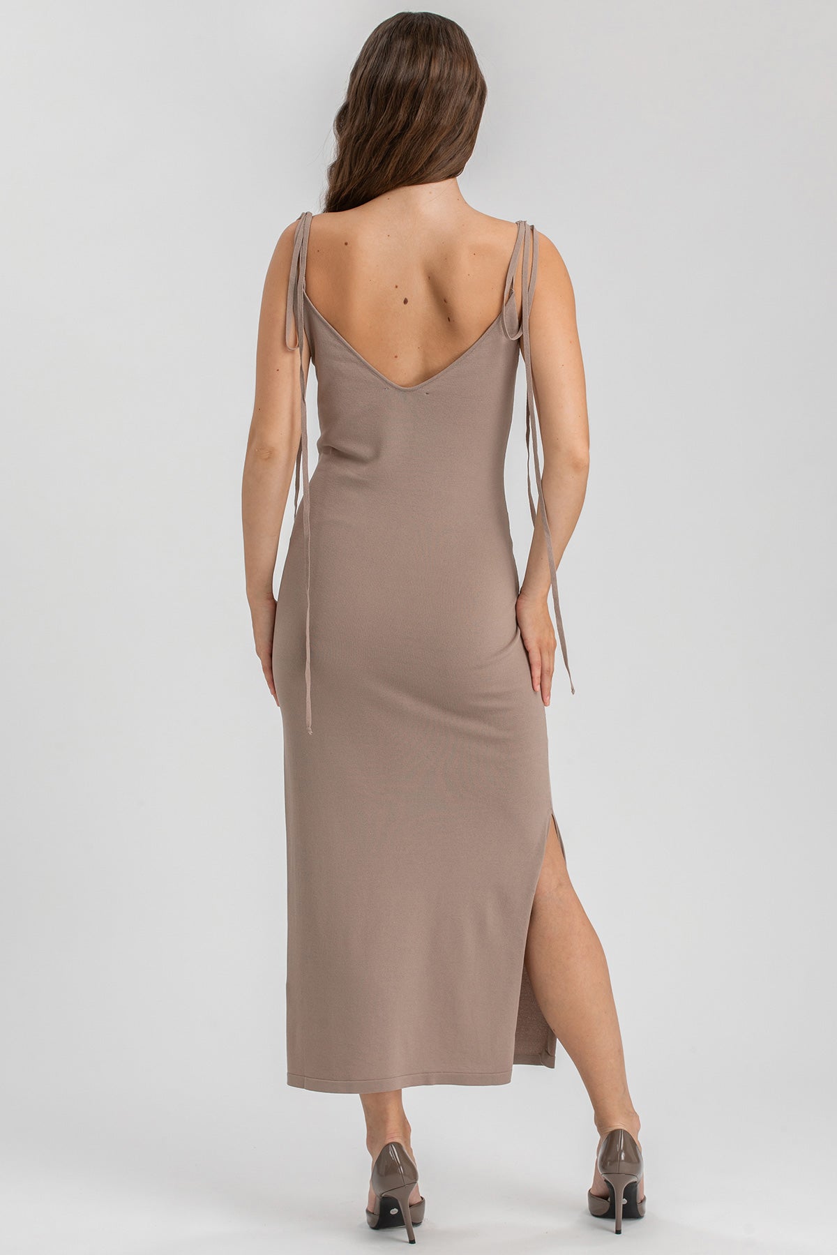 Donna di spalle con abito premaman lungo beige senza maniche e spacco laterale
