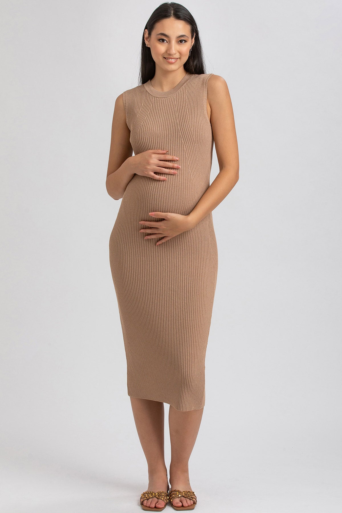 Donna incinta con abito premaman beige smanicato, tessuto a costine, fondo neutro.