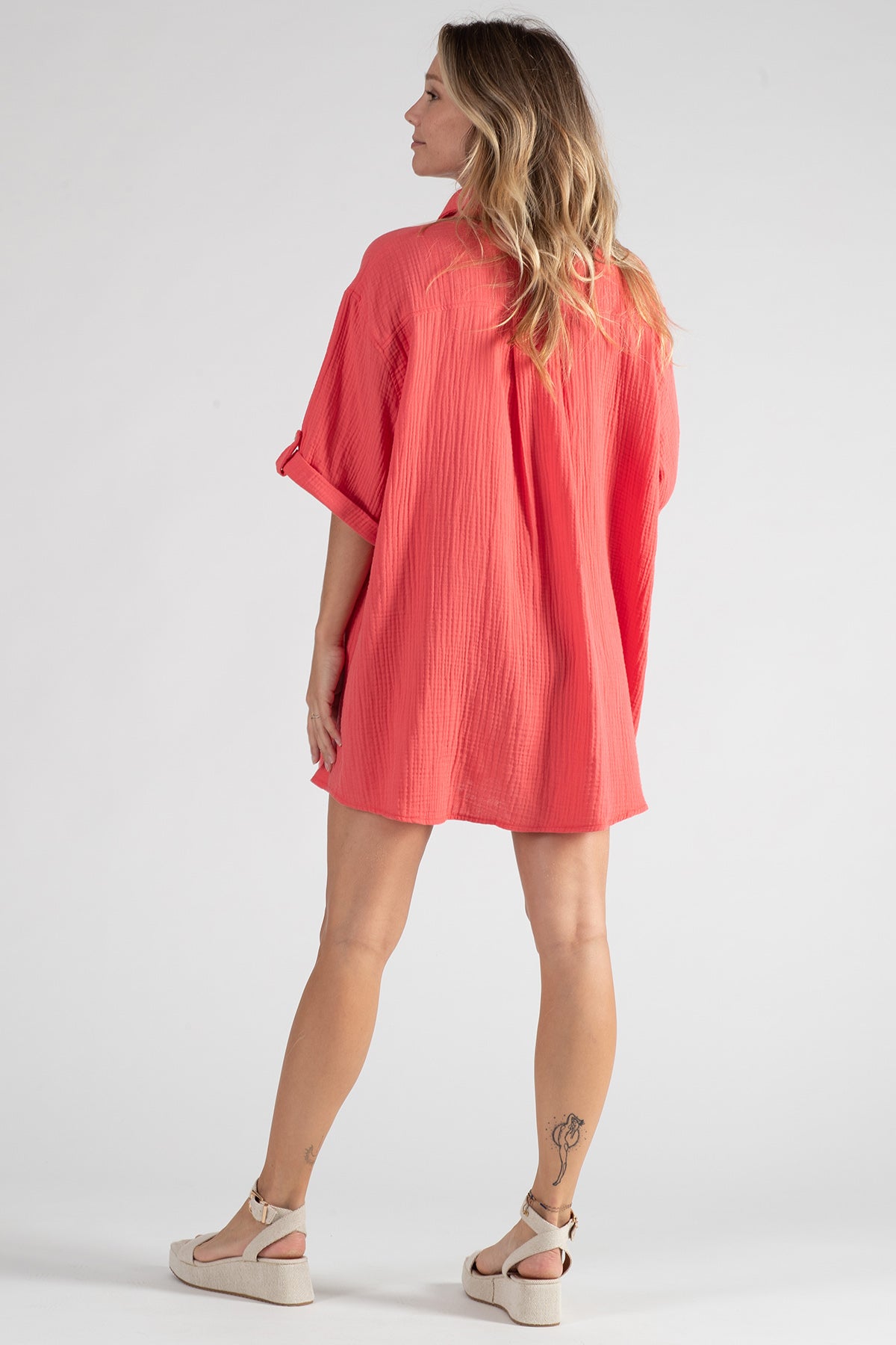 Donna di spalle con camicia premaman corallo maniche corte e sandali beige