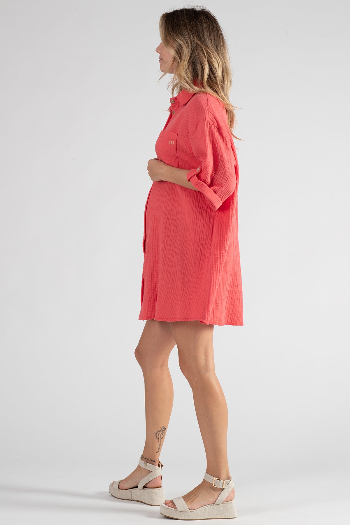 Donna incinta con abito premaman corto corallo a maniche lunghe e sandali beige
