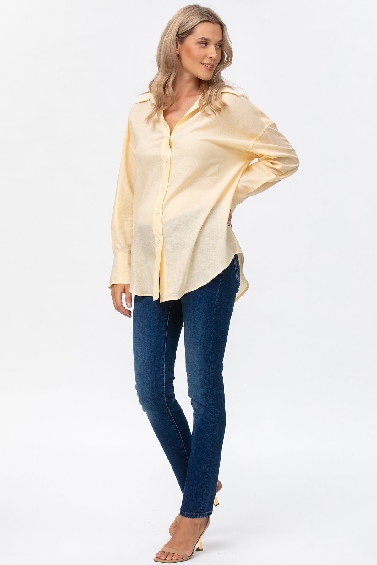 Camicia premaman gialla a manica lunga abbinata a jeans skinny, donna incinta in posa.