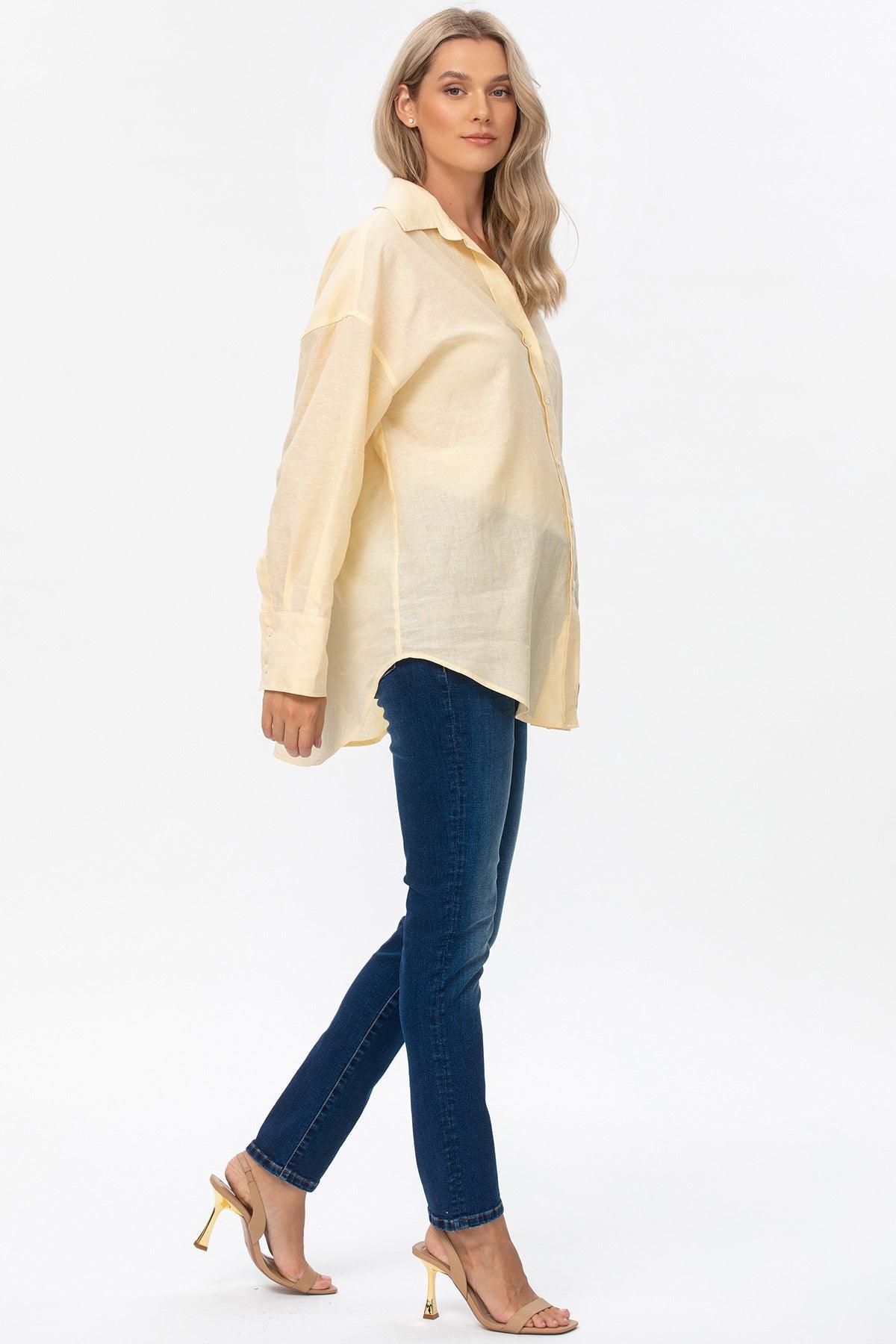 Donna incinta con camicia premaman gialla e jeans skinny blu su sfondo bianco