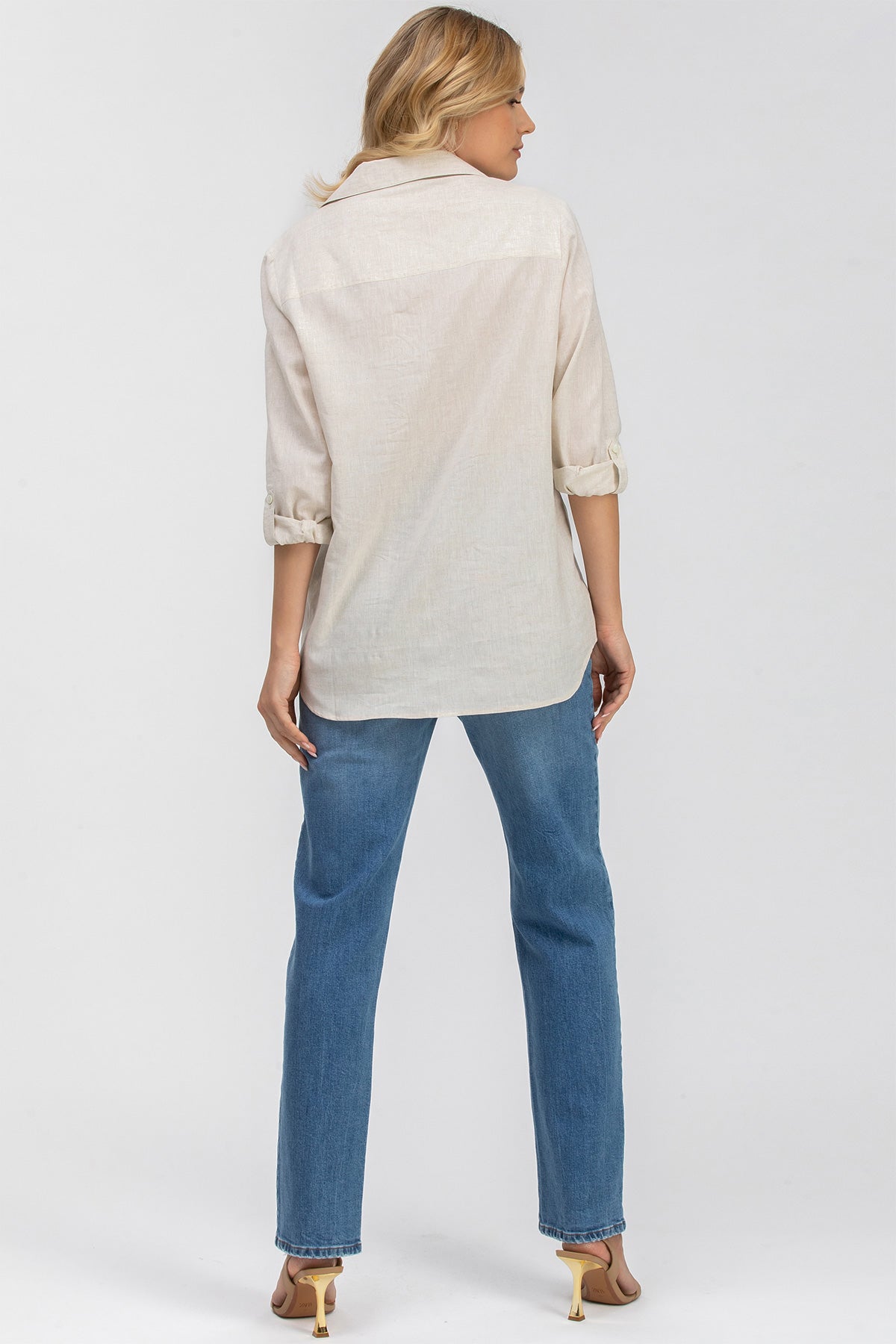 Donna di spalle con camicia lino beige maniche arrotolate e jeans premaman