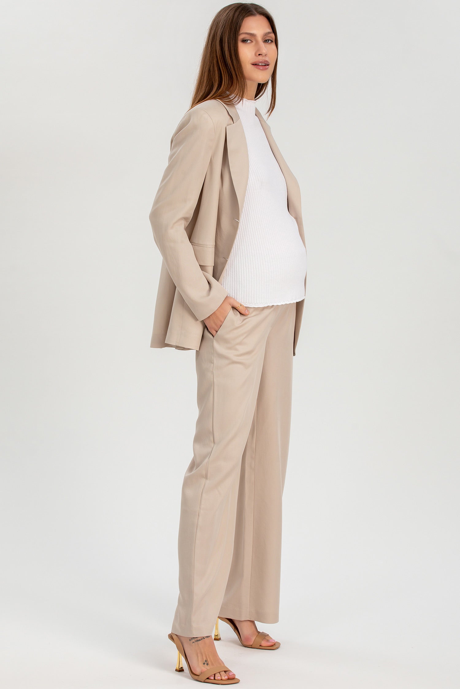 Donna incinta indossa tailleur premaman beige elegante con pantaloni larghi e top bianco.