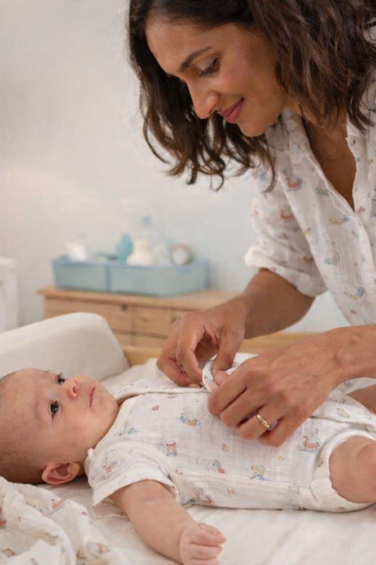 Mamma che veste un neonato su un fasciatoio, abbigliamento premaman comodo e pratico.