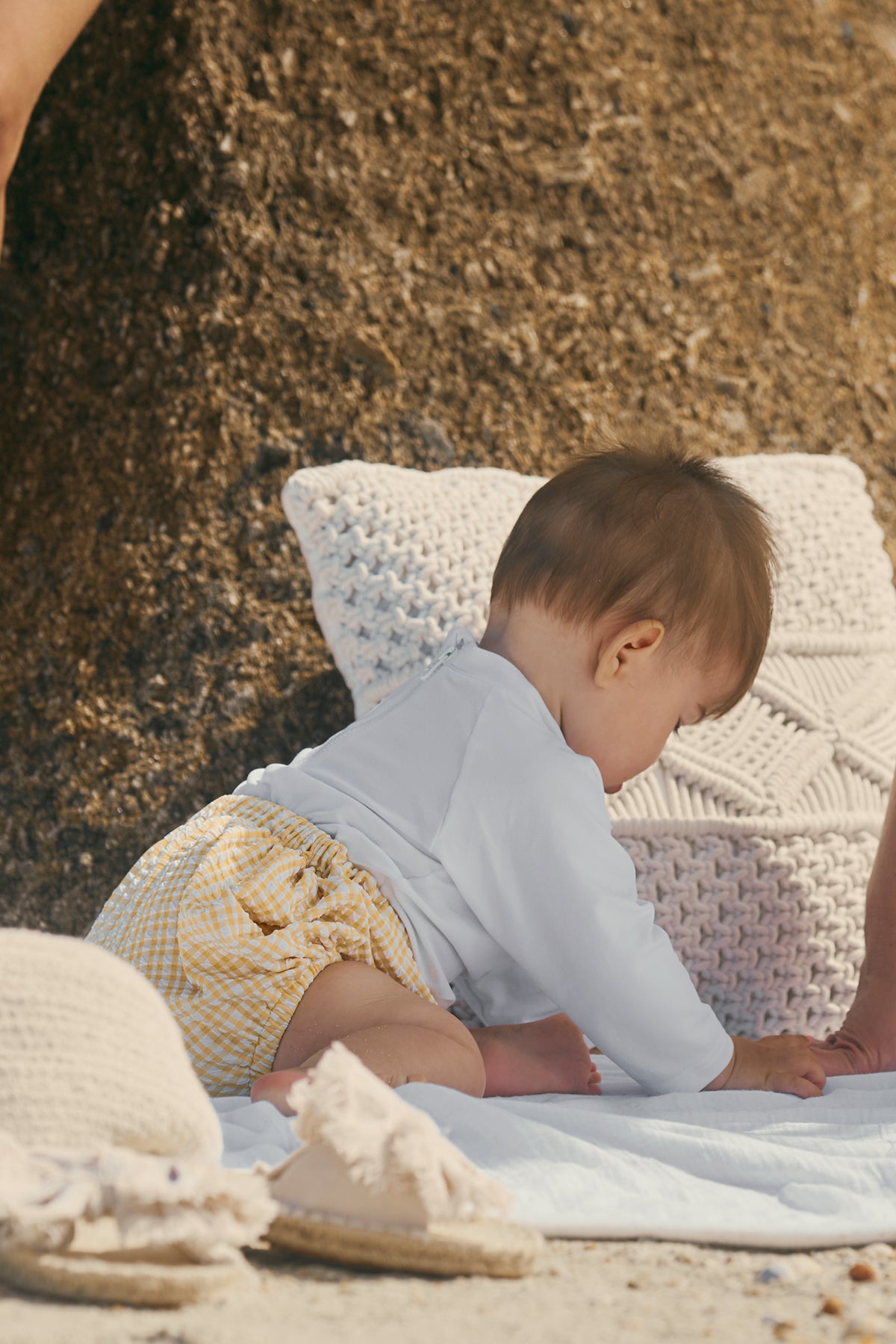 Bambino con maglietta bianca e shorts gialli a quadretti su coperta all'aperto