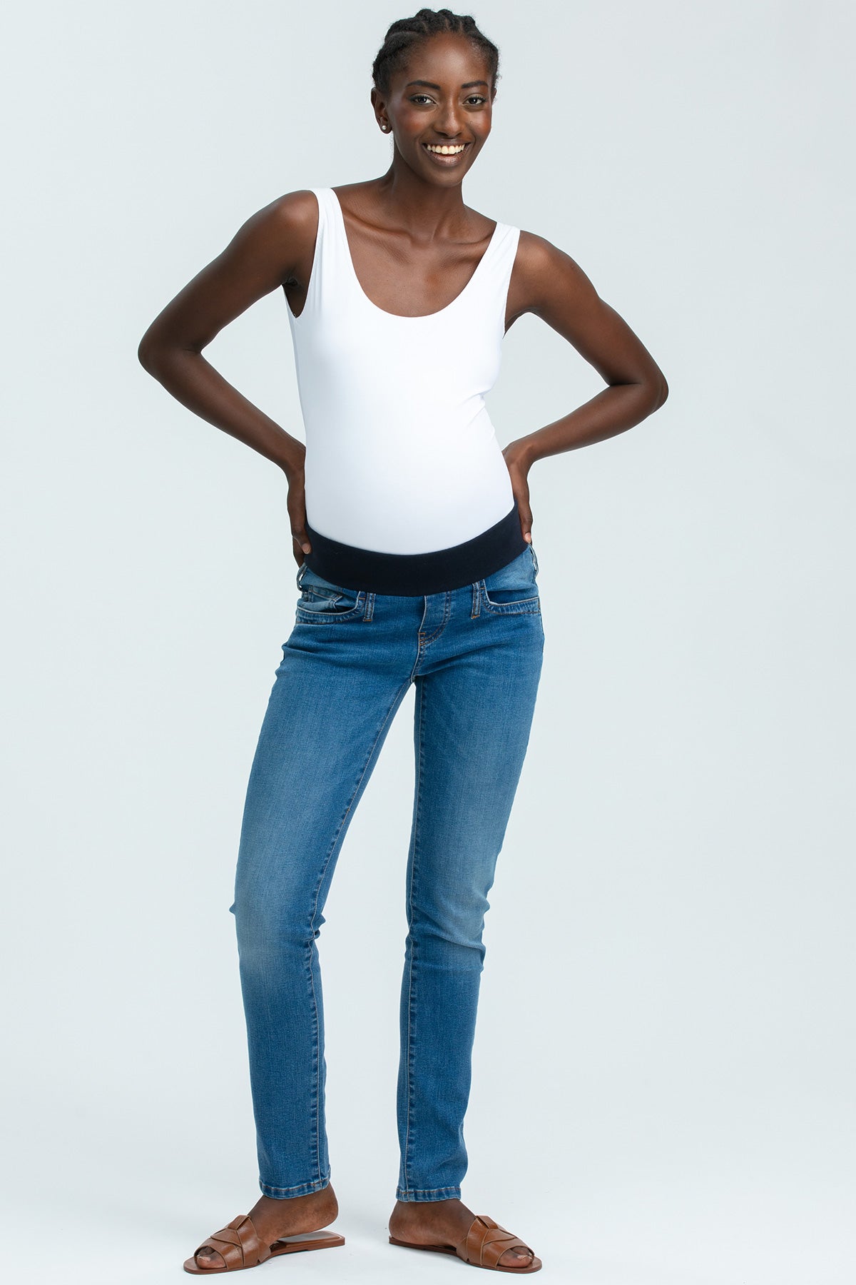 Donna sorridente con jeans premaman skinny e canotta bianca, moda abbigliamento premaman.
