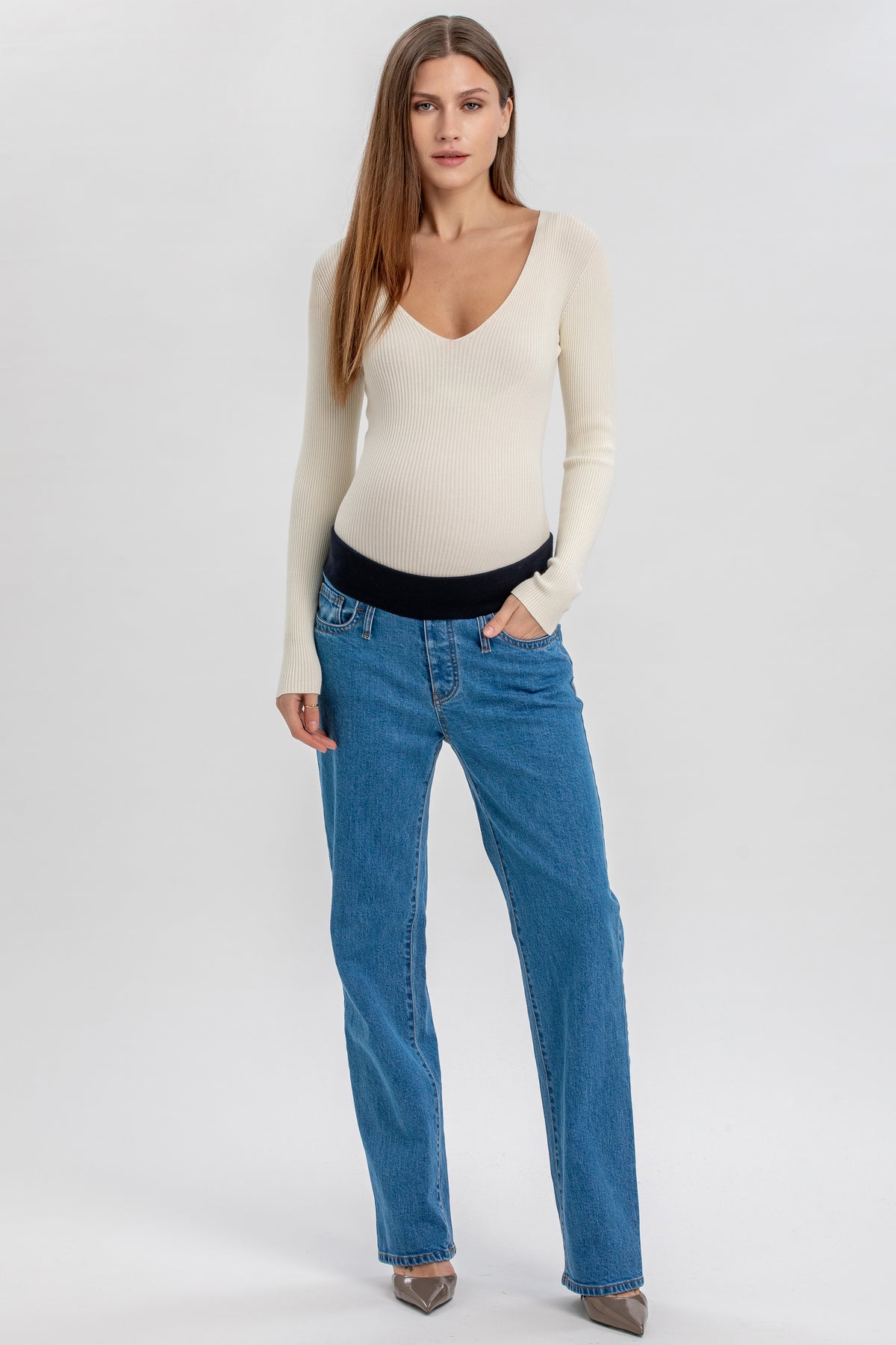 Modella indossa jeans premaman blu a gamba dritta con fascia elastica e maglia panna con scollo a V