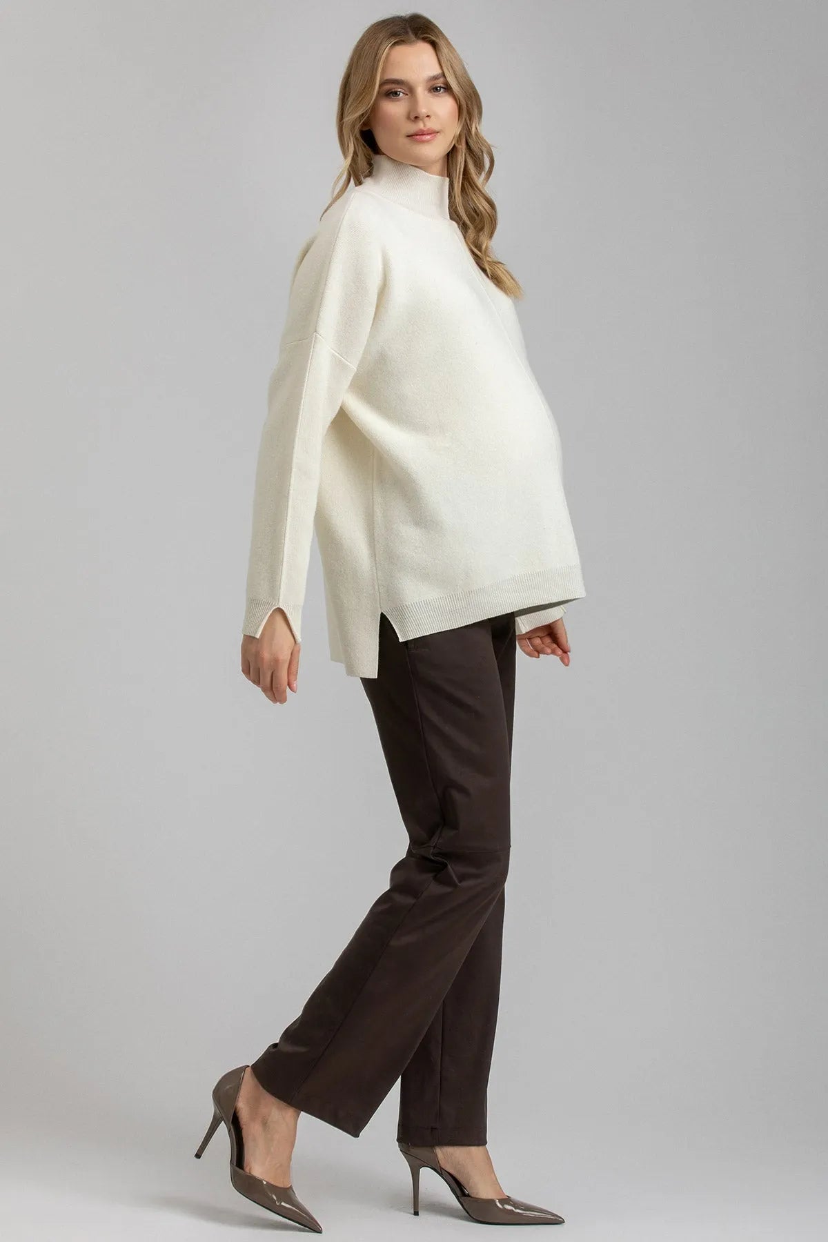 Donna incinta indossa maglione premaman bianco e pantaloni marroni eleganti
