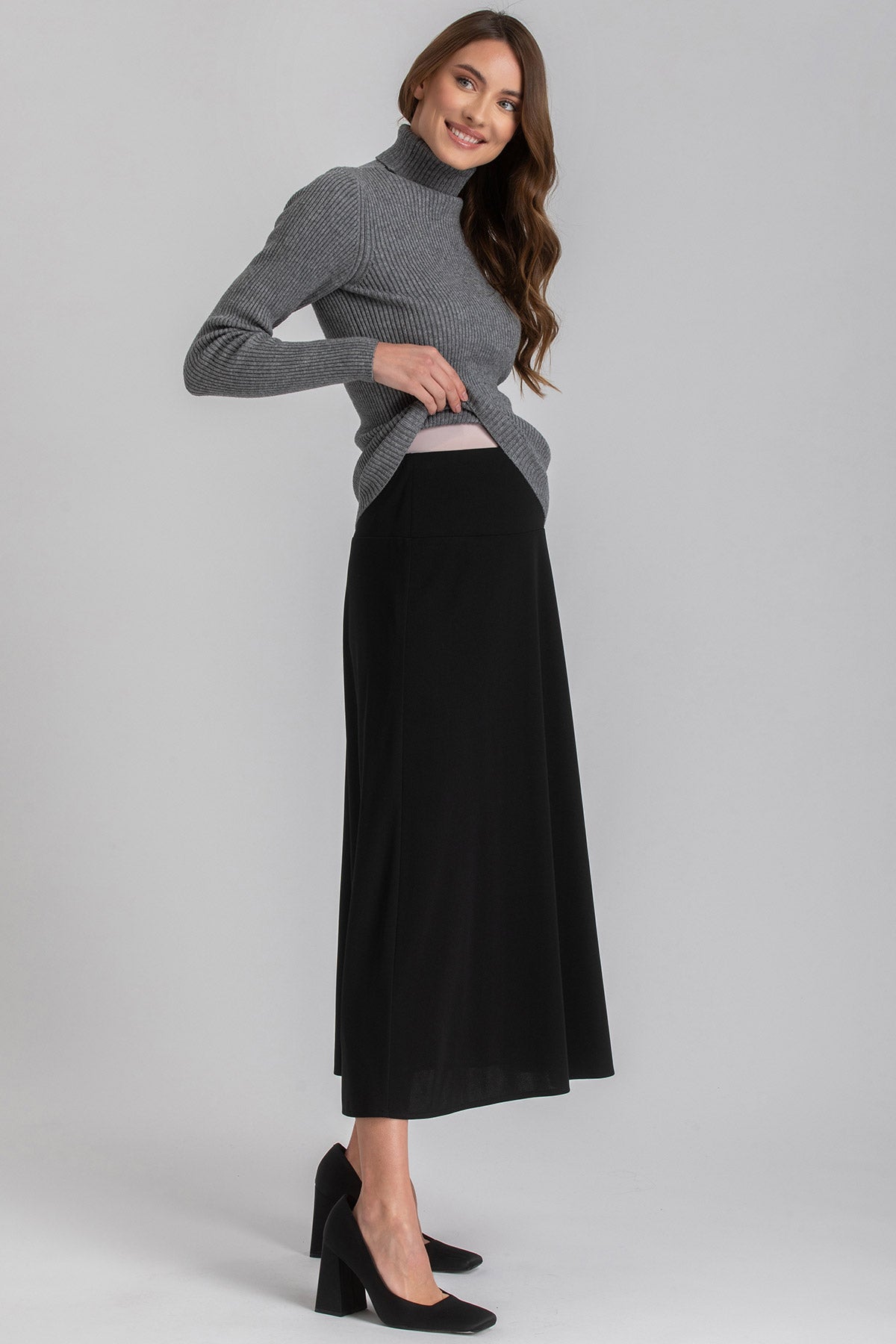 Donna che indossa gonna premaman nera lunga e maglione grigio, abbigliamento premaman elegante