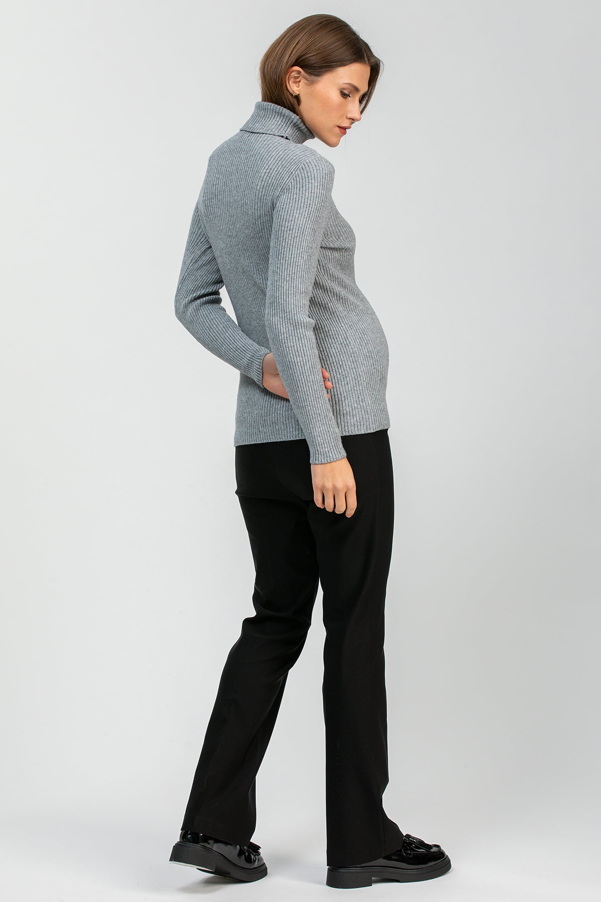 Donna incinta indossa maglione premaman grigio a coste e pantaloni neri eleganti