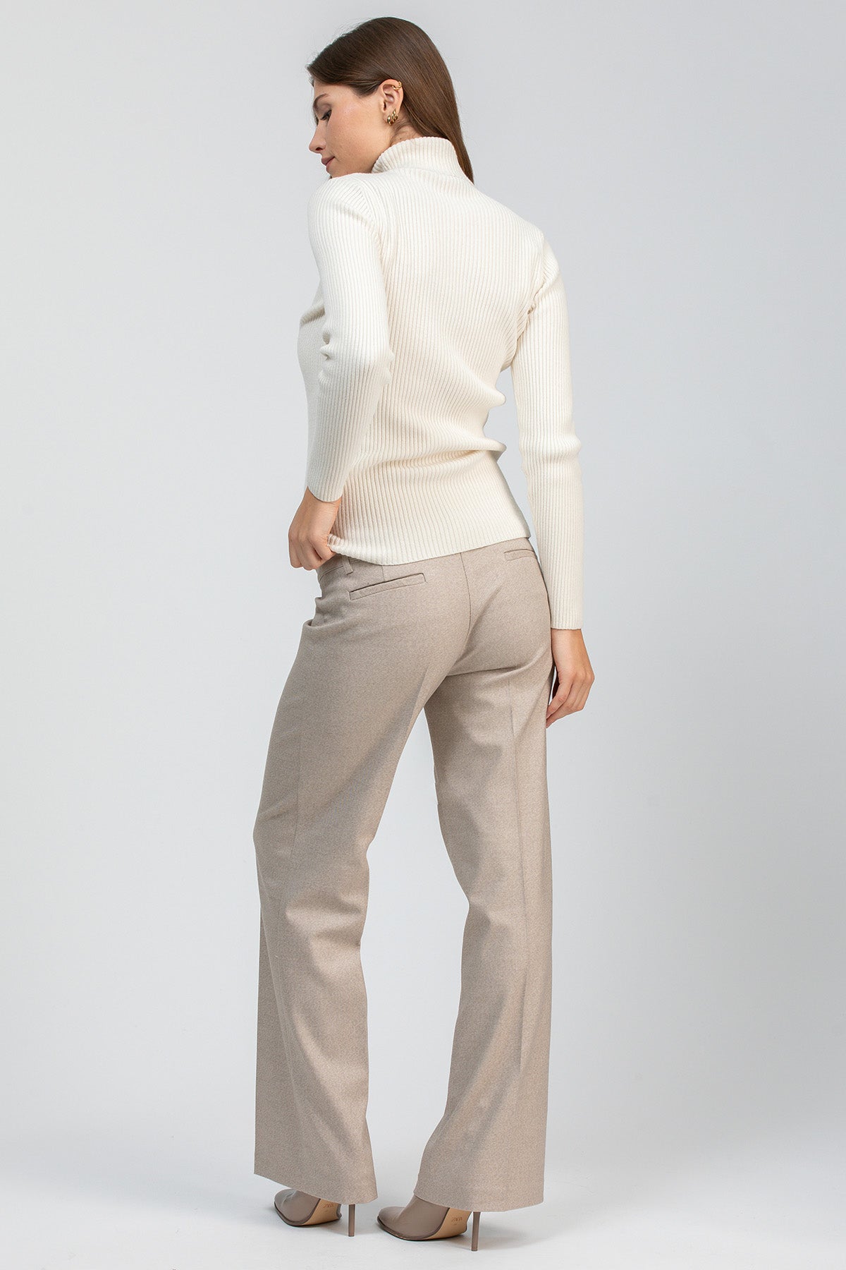 Modella con maglia premaman bianca a collo alto abbinata a pantaloni beige a gamba dritta