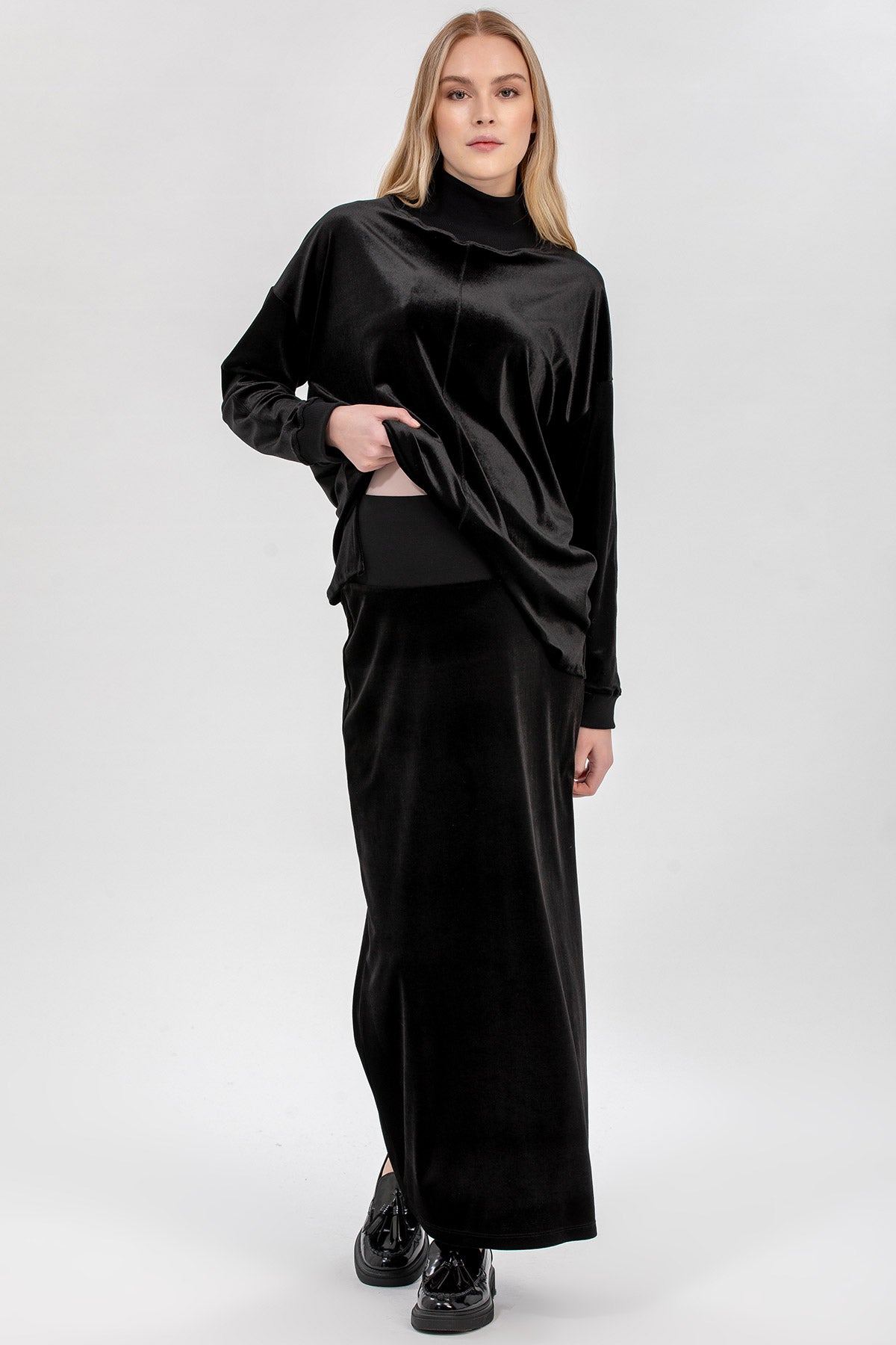 Modella indossa abbigliamento premaman elegante nero in velluto, maglia e gonna lunga.