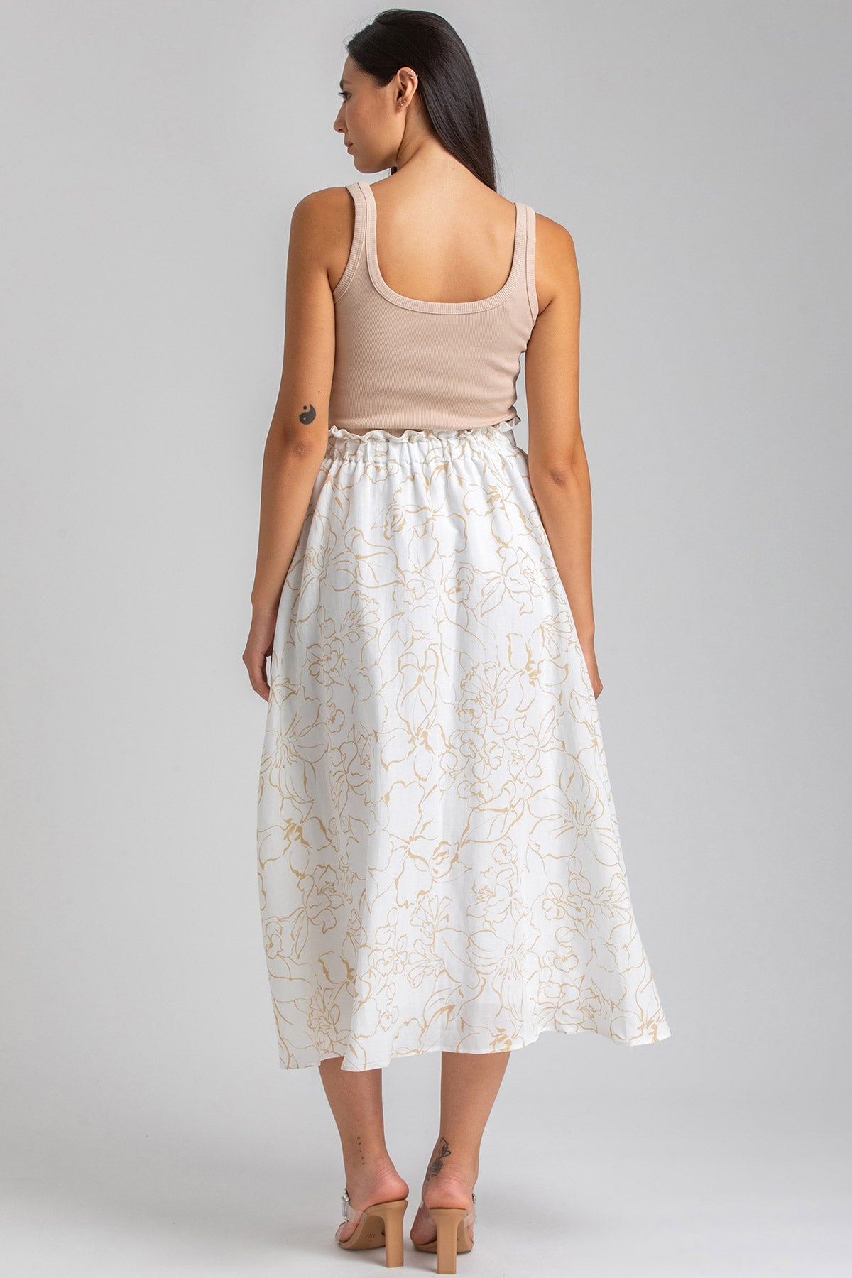 Donna di profilo con top beige e gonna lunga bianca premaman a fantasia floreale