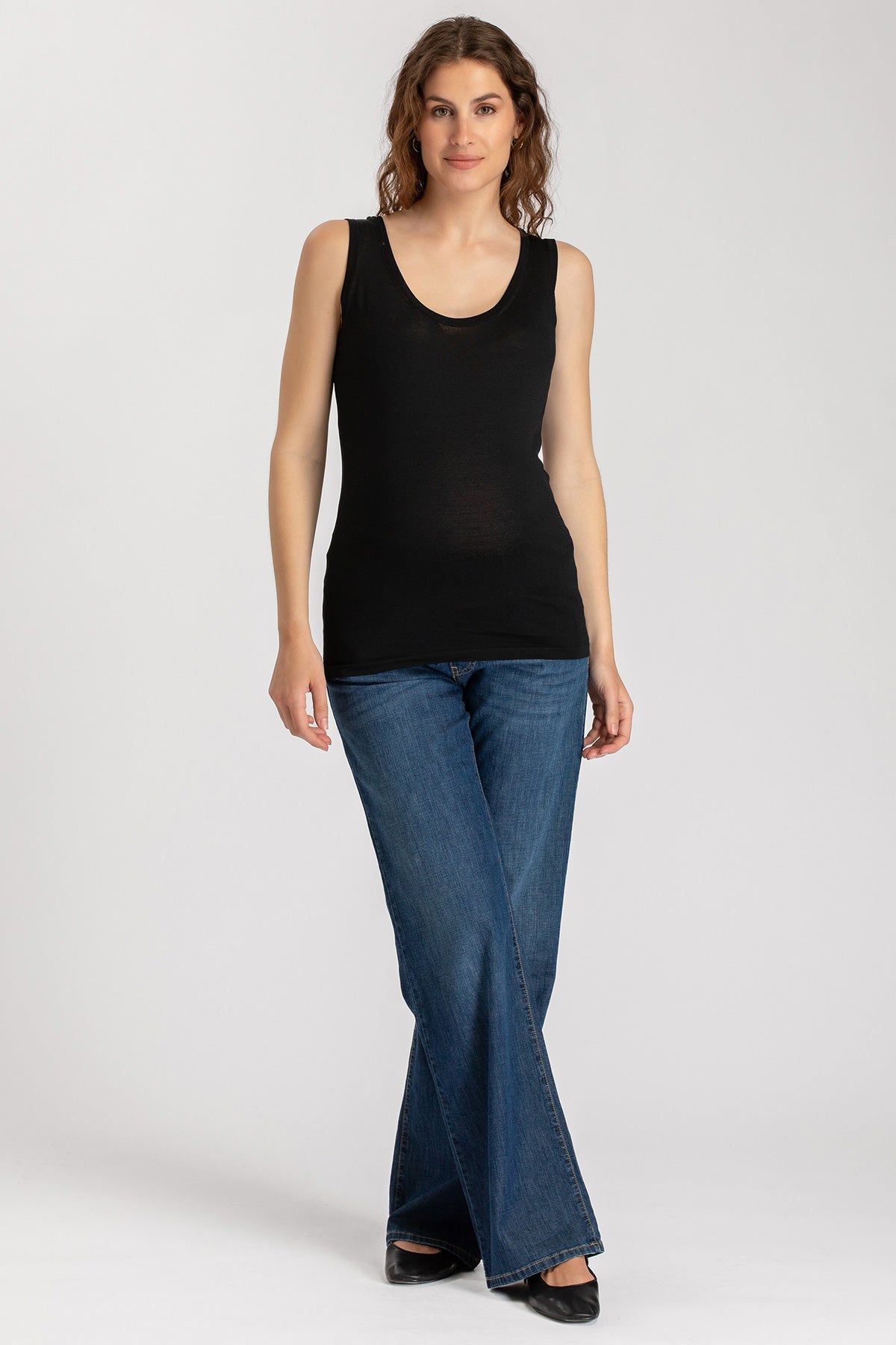 Modella indossa top premaman nero senza maniche e jeans premaman a zampa, stile casual.