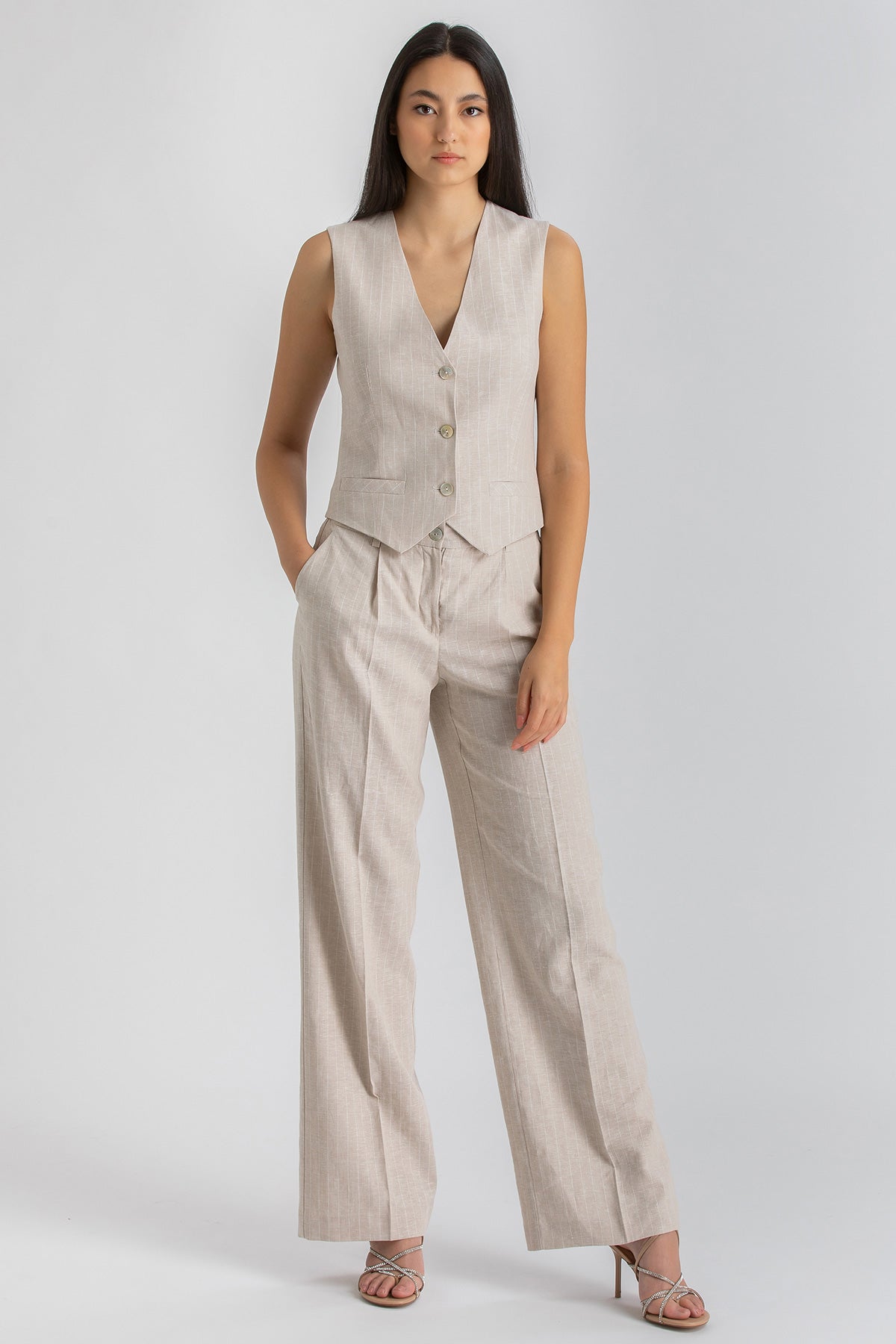 Donna indossa completo premaman beige elegante con pantaloni ampi e gilet, moda premaman.