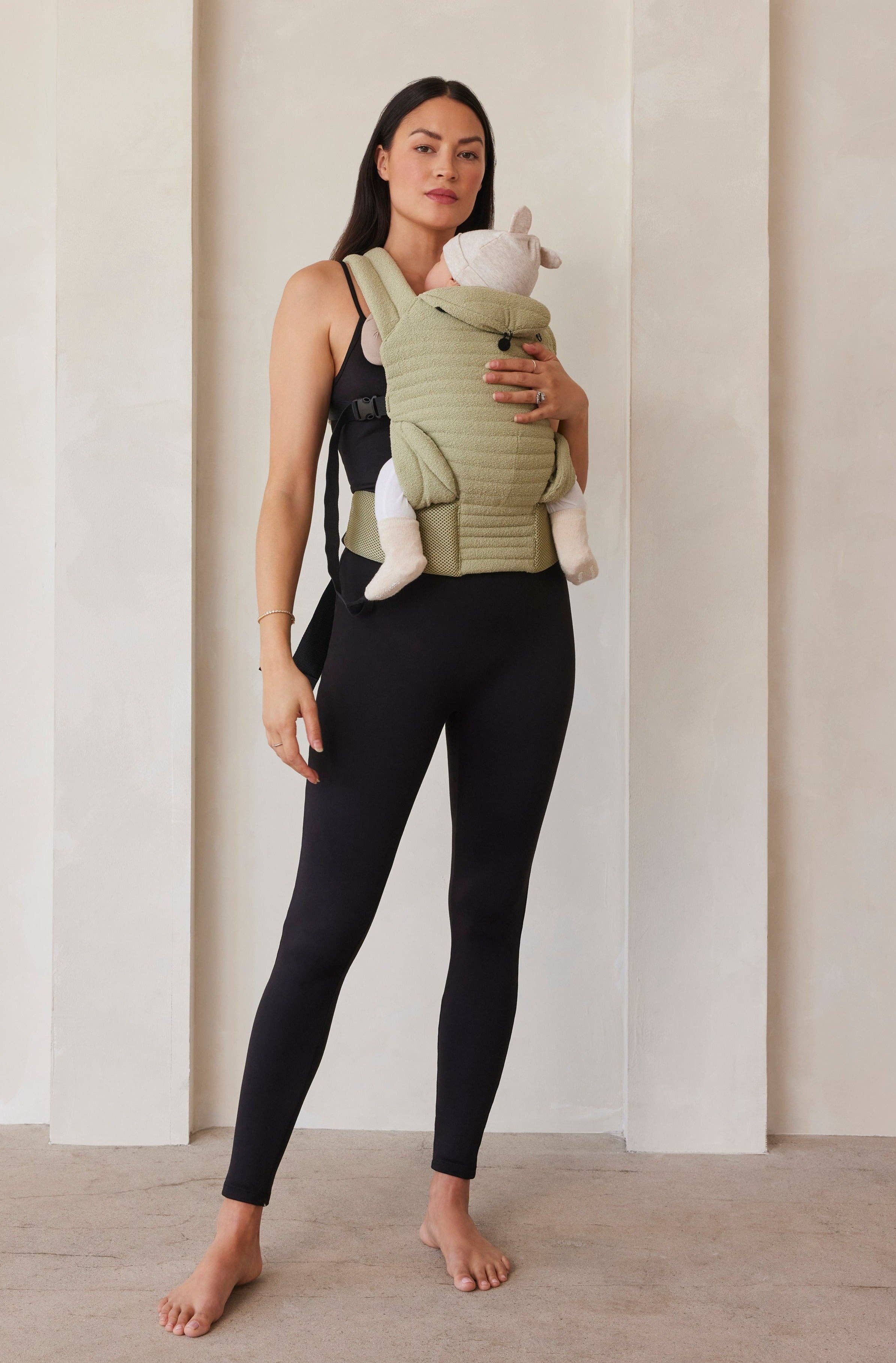 Donna in leggings premaman neri porta un bambino in marsupio; abbigliamento premaman elegante