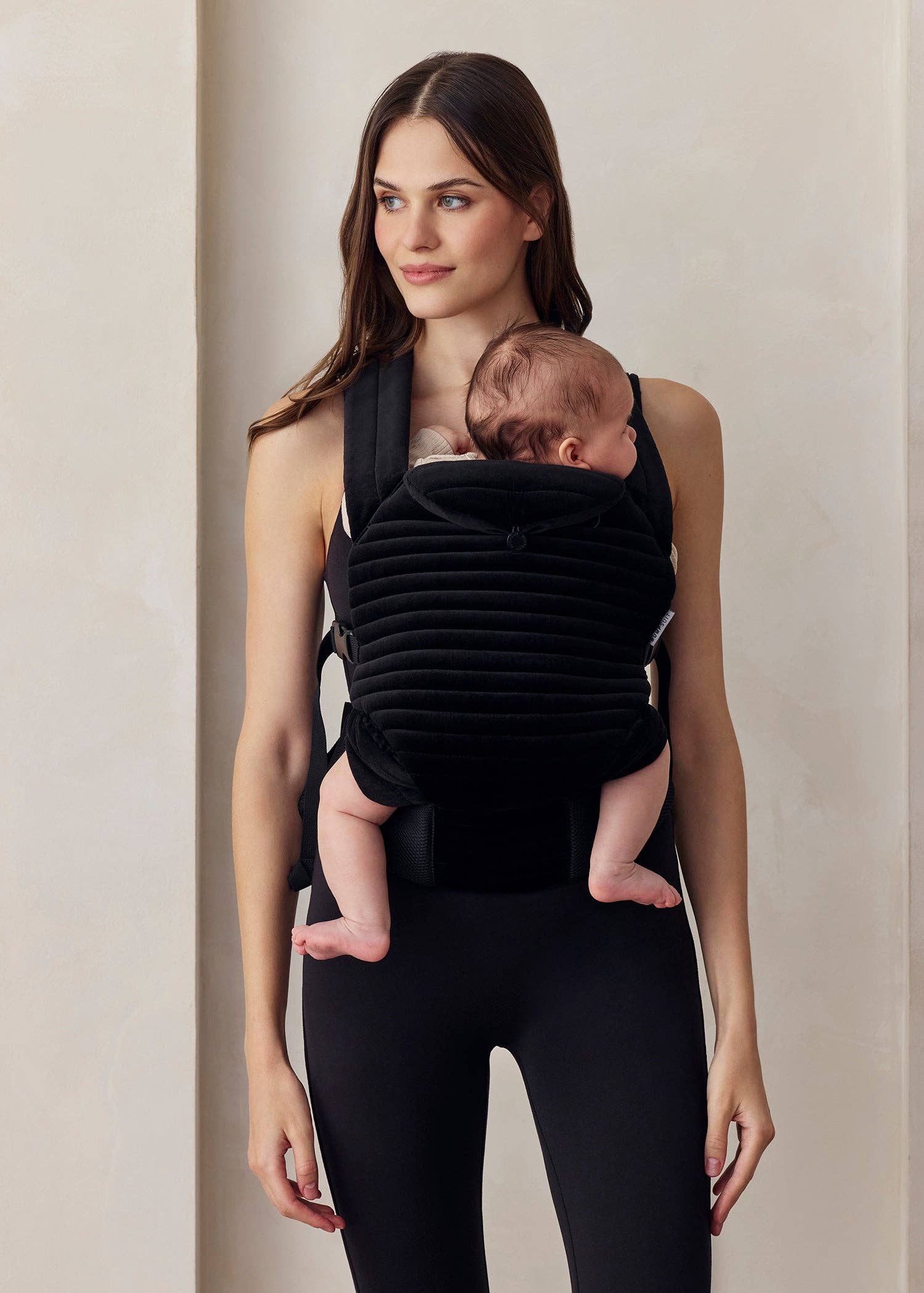 Donna con bambino in marsupio nero, abbigliamento premaman elegante e confortevole