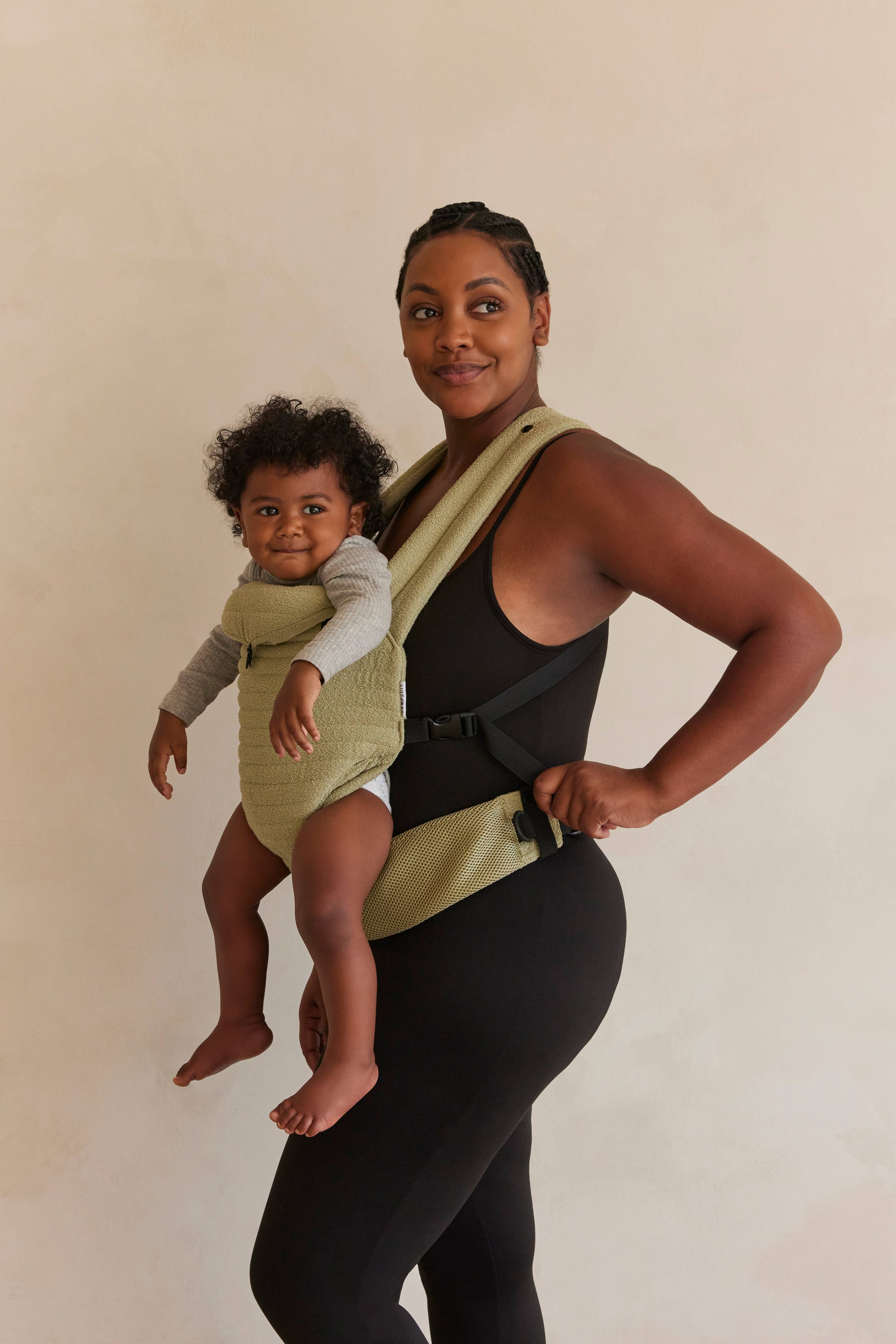 Mamma in abbigliamento premaman nero con marsupio porta bebè verde e bambino sorridente