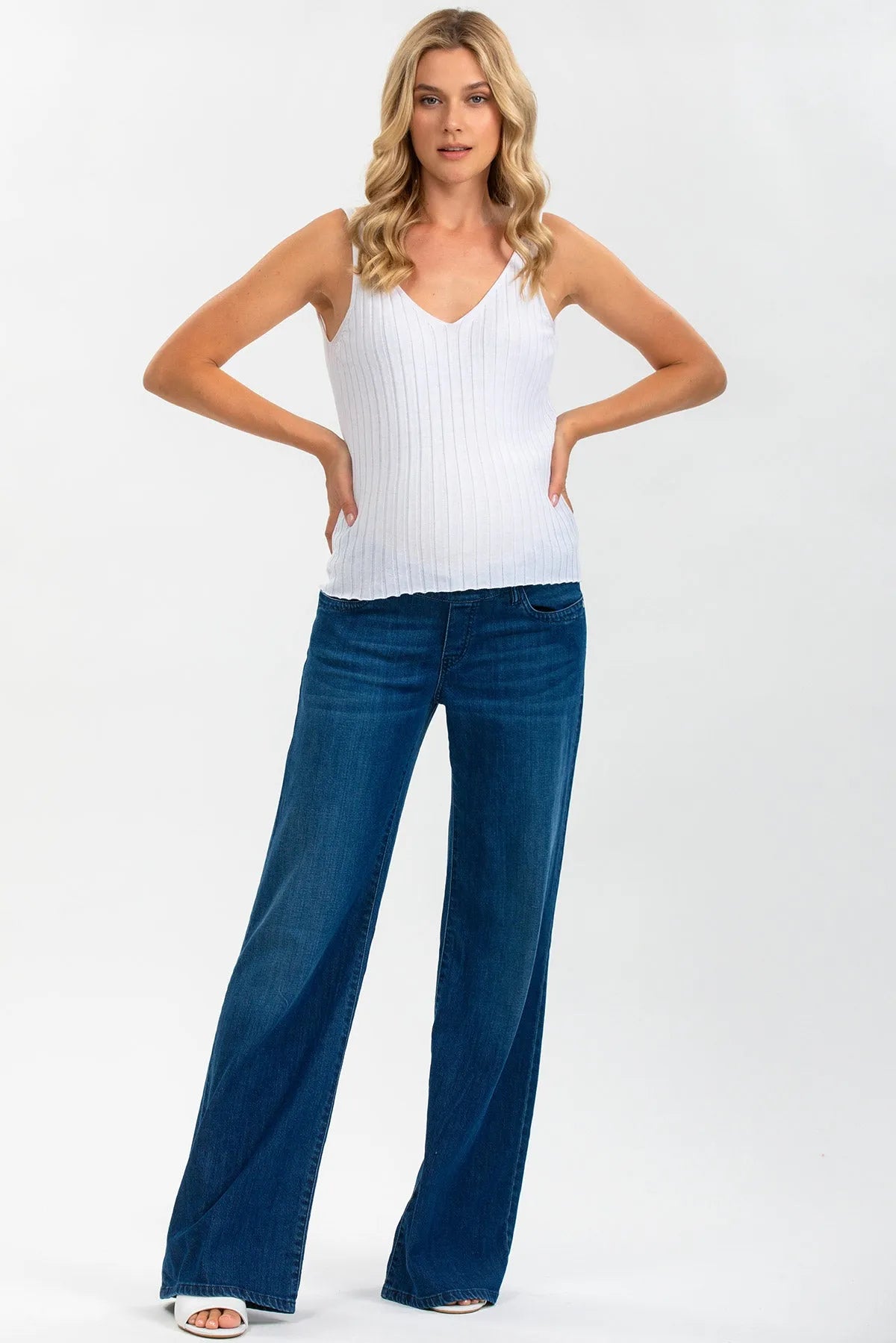 Donna incinta indossa top premaman bianco a coste e jeans flare blu, moda gravidanza elegante.